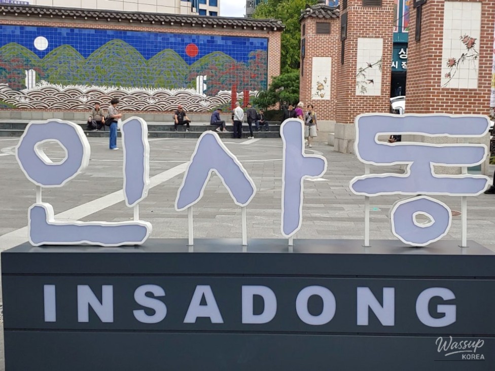 A vibrant, busy street scene in Insadong featuring traditional architecture and crowds of tourists