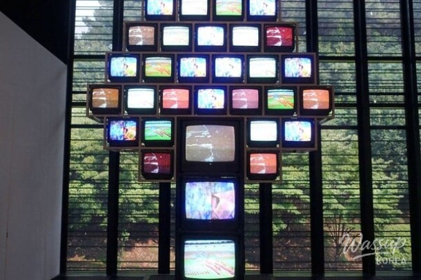 Antique televisions placed among lush green plants in the TV Garden exhibition