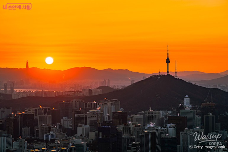 A crowd of people gathered on a Seoul mountain peak waiting for the sunrise with glowing lanterns
