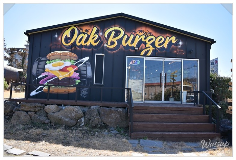 Oak-themed interior with Jeju stone walls and palm trees creating a cozy handmade burger restaurant atmosphere