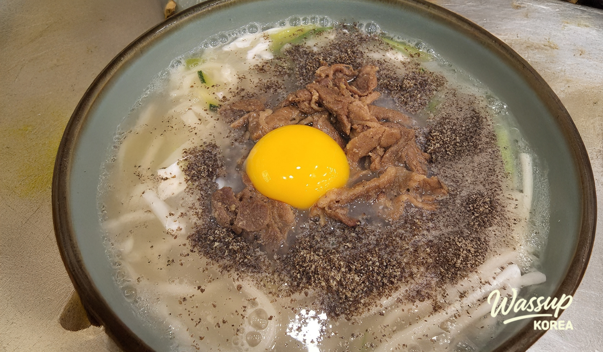 Hearty bowl of charcoal-grilled meat kalguksu with a fresh egg yolk